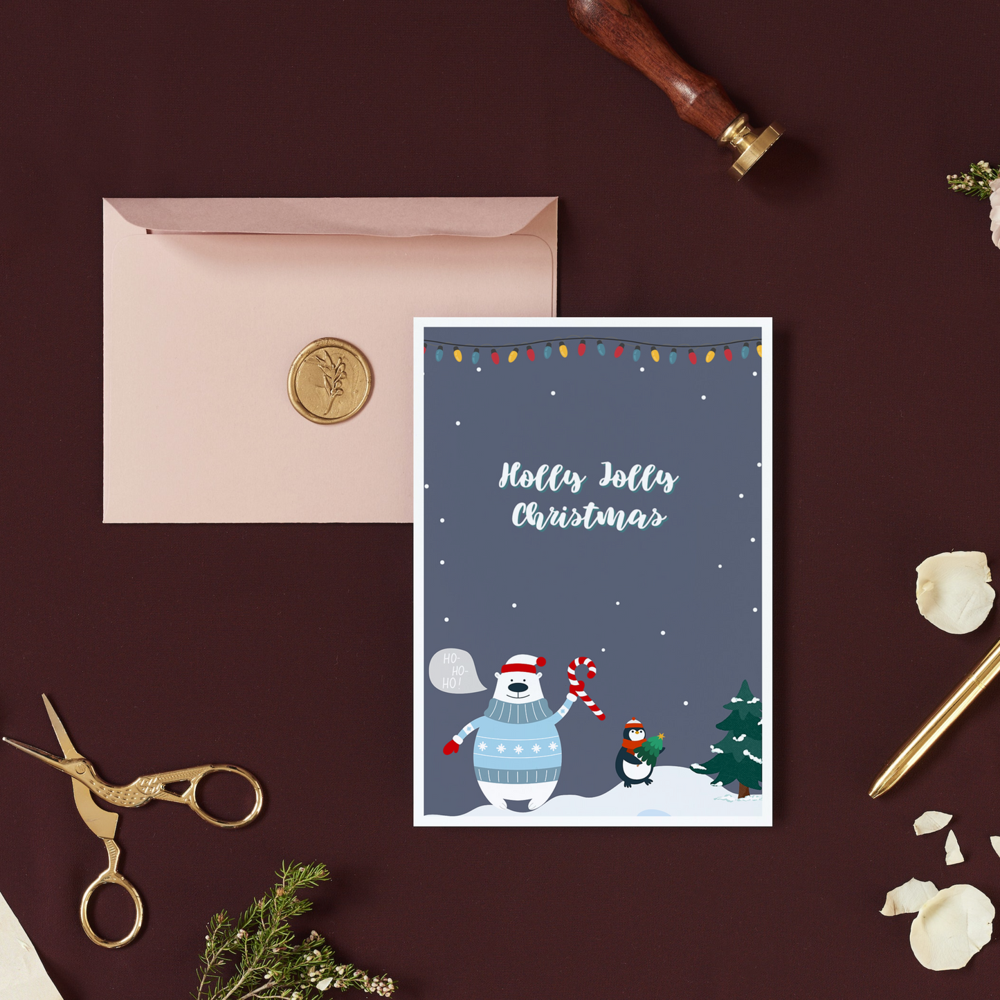 A Christmas card featuring an illustration of a polar bear and penguin in a snowy setting, with 'Holly Jolly Christmas' text, placed on a desk with a pink envelope and a gold-colored pen.